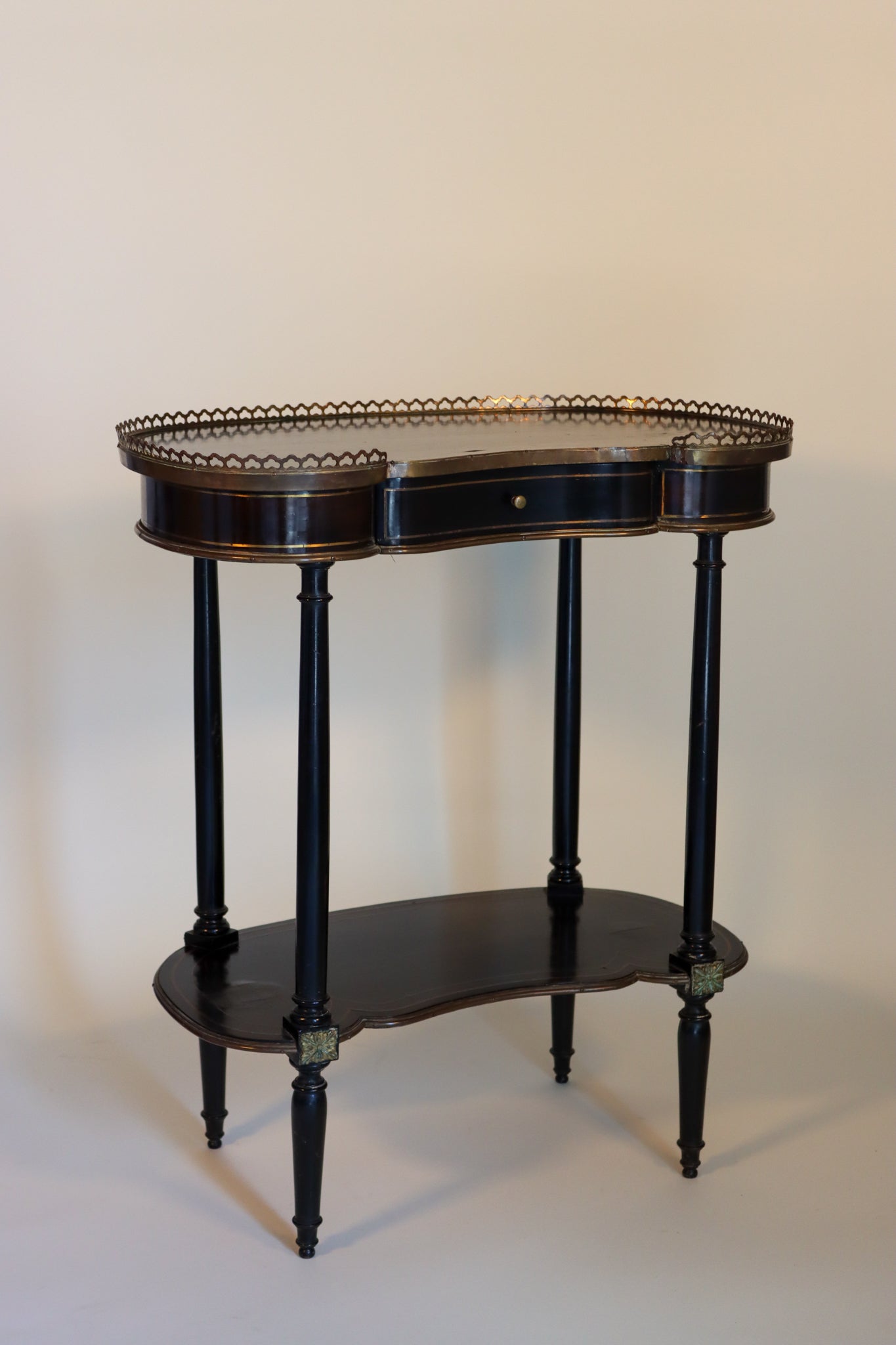 A black kidney-form table with gilt-metal accents, the top with central drawer, raised on four legs with a medial shelf.