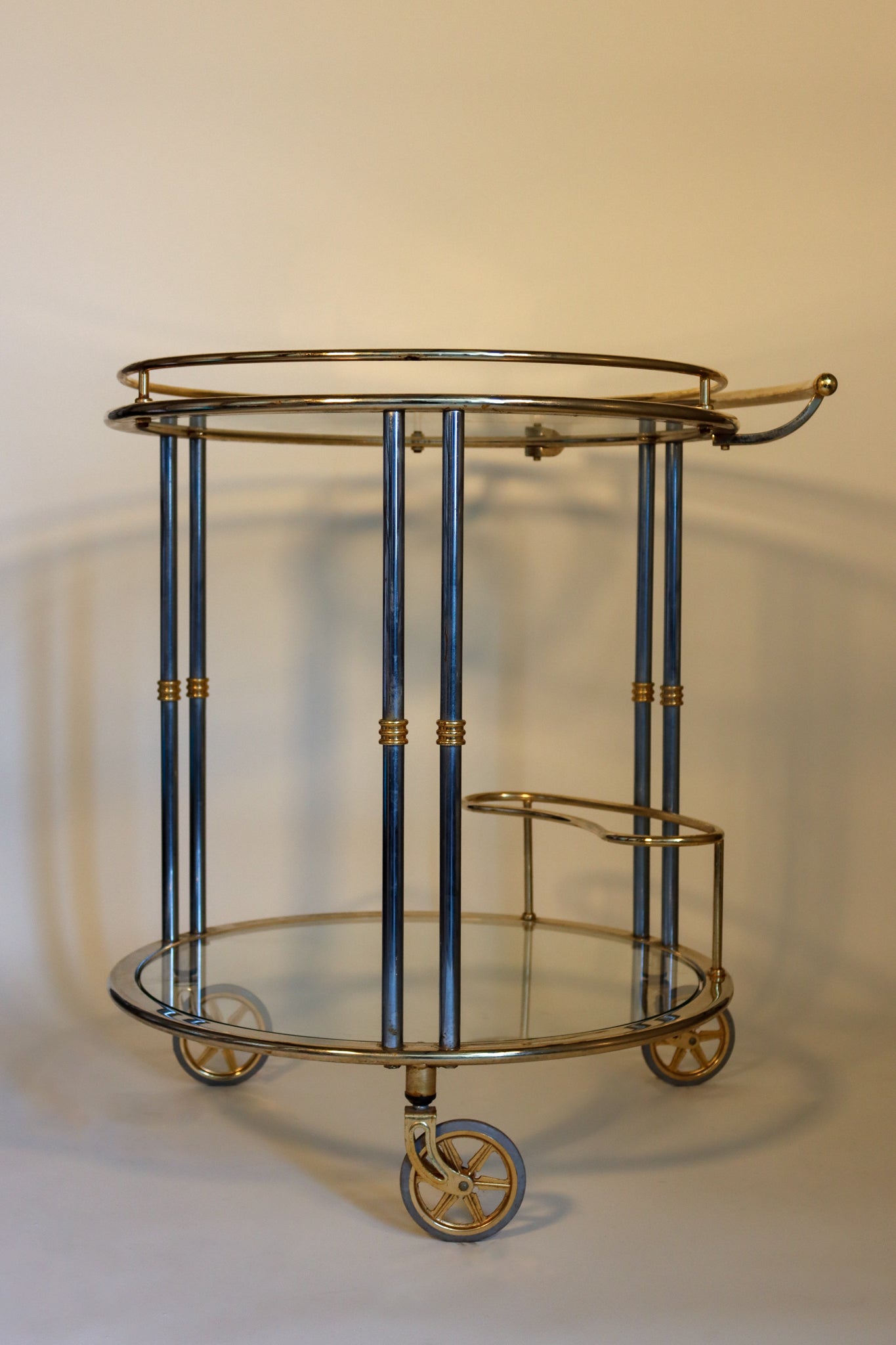 A chrome, brass, and glass bar cart with two round shelves, wine bottle holder, and three wheels.