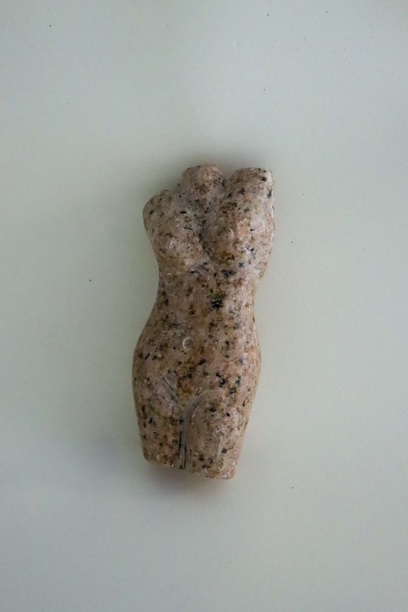 A carved stone or granite female torso, the stone with speckled coloring against a light pink ground, formed in a slight contrapposto.