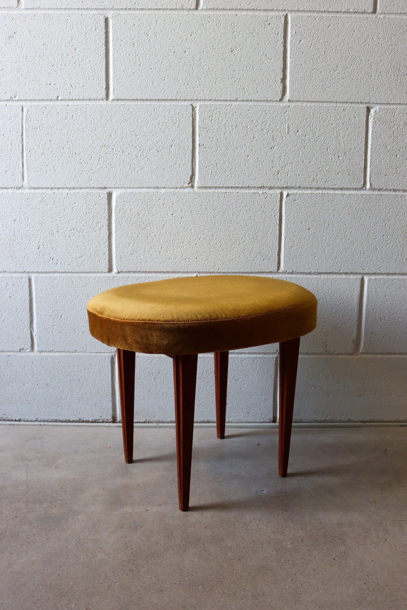 A stool formed as an oval ochre velvet seat over four tapering teak legs.