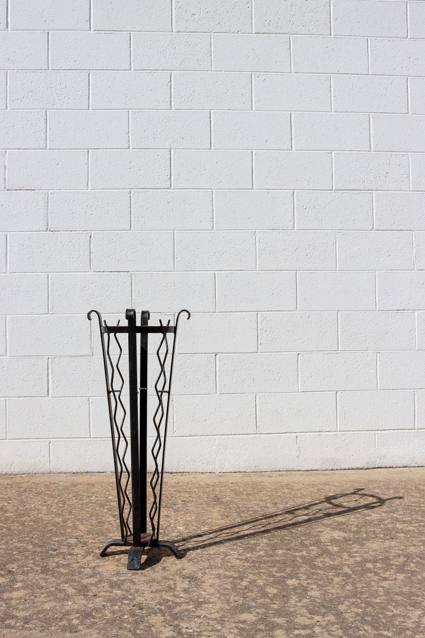 A black painted jardiniere plant stand with alternating vertical straight and squiggle lines casts a long shadow.