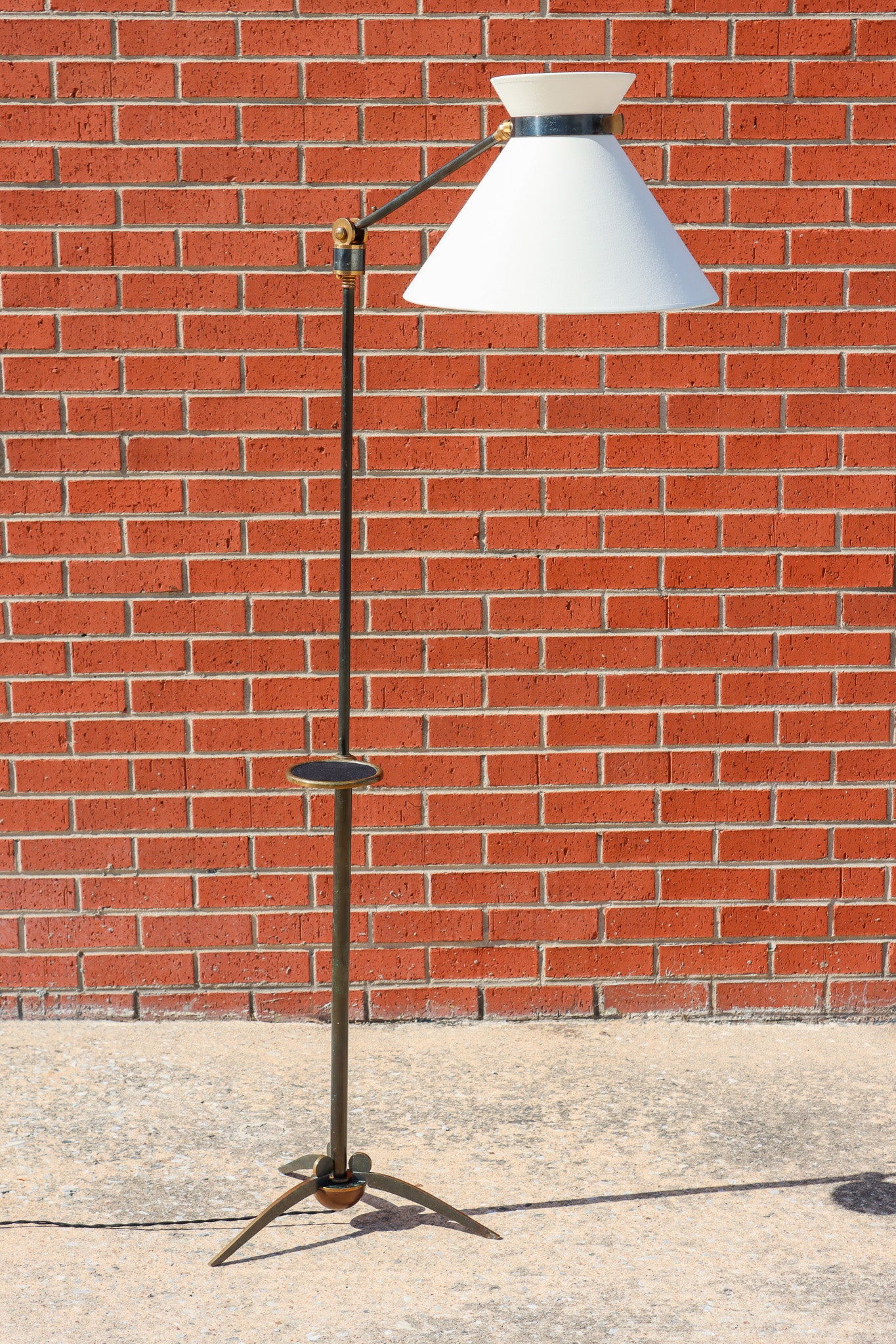 An adjustable black metal lamp with a drink holder and white shade against a brick wall.